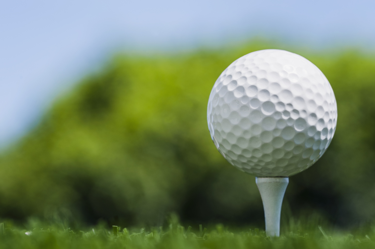 Low angle of a Golf Ball on wooden white tee against trees and blue sky